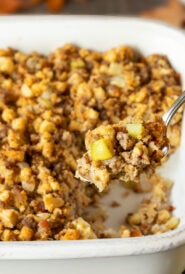 White baking dish filled with Apple Sausage Stuffing with a spoon holding a scoop