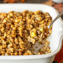 White baking dish filled with Apple Sausage Stuffing with a spoon holding a scoop
