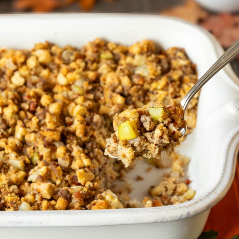White baking dish filled with Apple Sausage Stuffing with a spoon holding a scoop