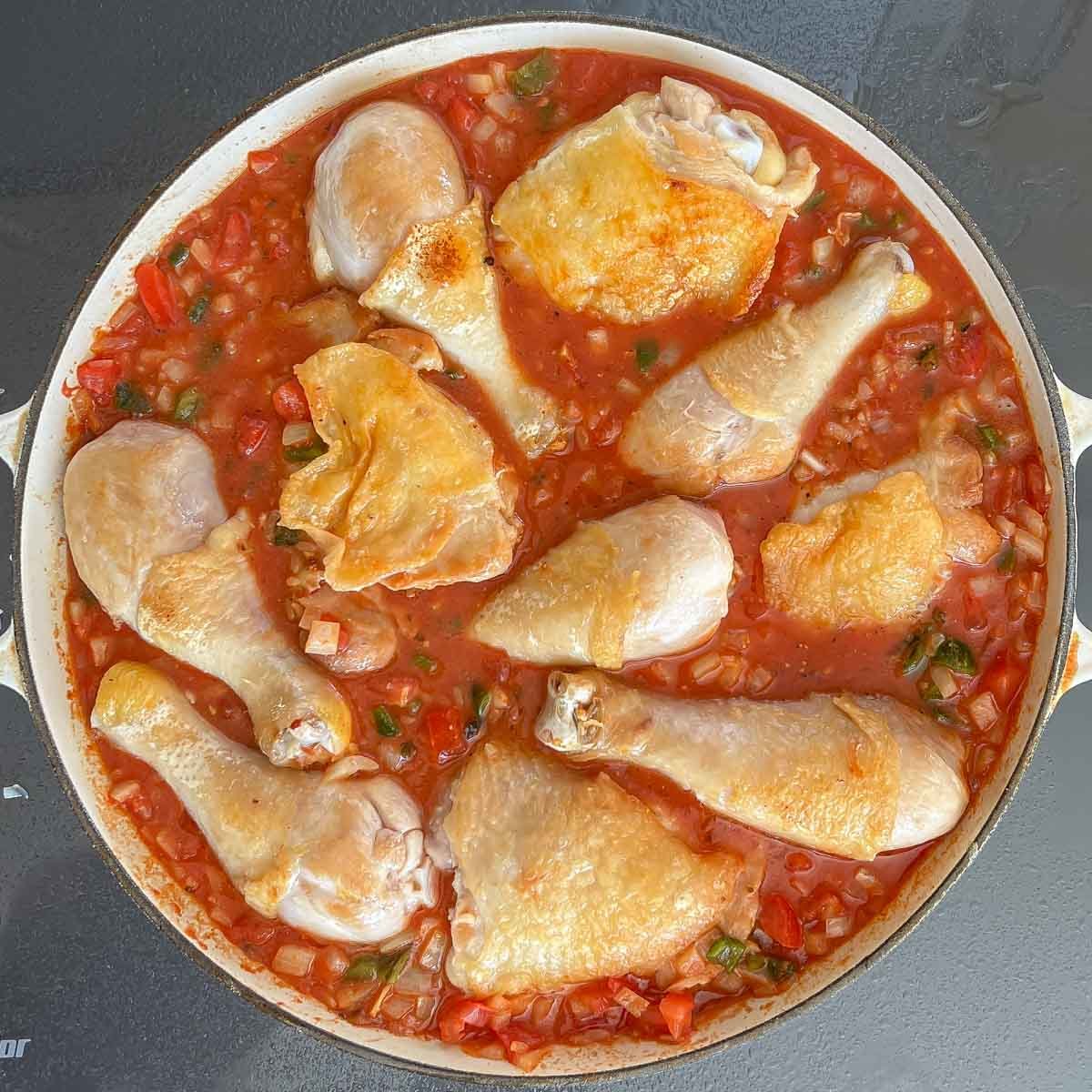 Arroz con Pollo rice and sauce in shallow baking dish with browned chicken pieces on top, ready for baking