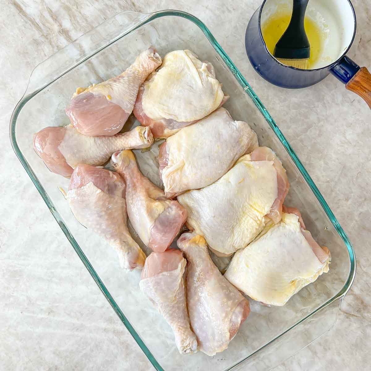 raw chicken pieces in a dish that have been brushed with the garlic olive oil
