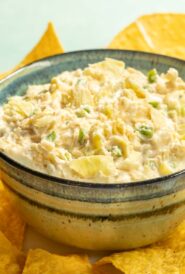 Blue striped bowl holding Jalapeno Artichoke Dip, surrouded by tortilla chips