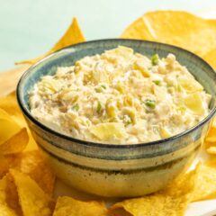 Blue striped bowl holding Jalapeno Artichoke Dip, surrouded by tortilla chips