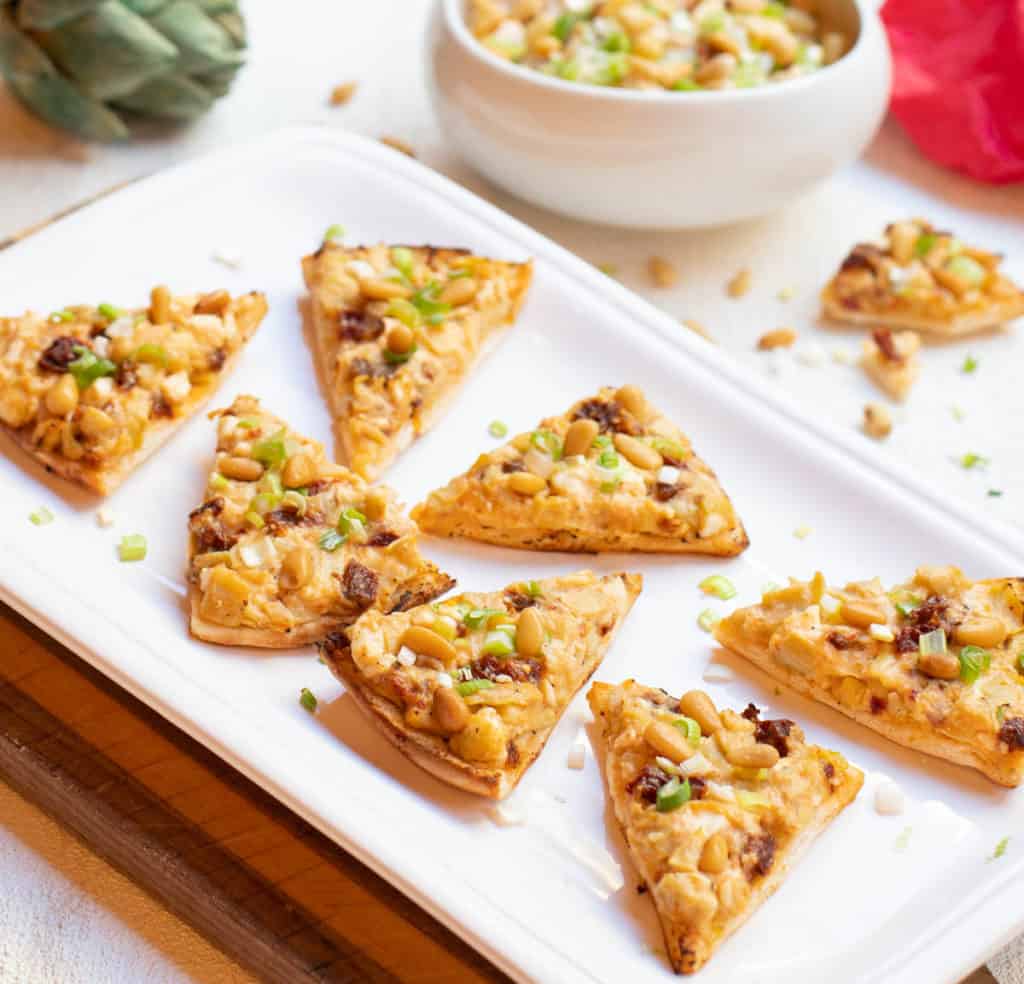 Artichoke, sun-dried tomato and feta triangles on plate, next to same ingredient dip