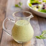 Arugula Salad Dressing in a clear glass pitcher with a salad in the background