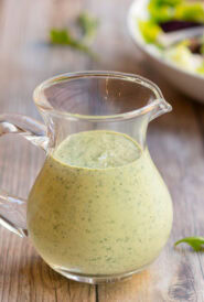 Arugula Salad Dressing in a clear glass pitcher with a salad in the background