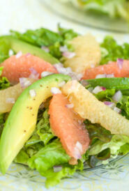 Individual serving of Avocado Grapefruit Salad with slices of avocado, pink, and white grapefruit alternating in a pinwheel on greens