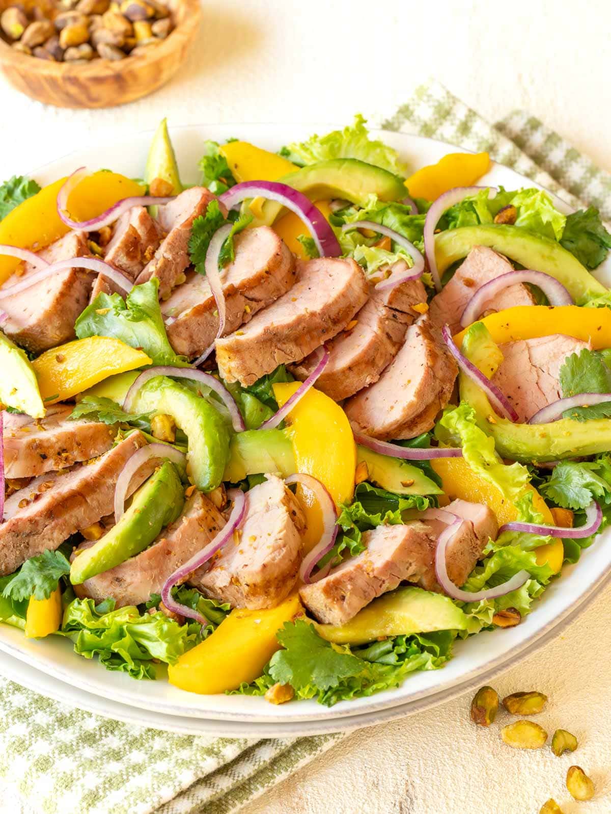 White platter holding Avocado Mango Salad with Pork Tenderloin, with bowl of pistachios in background