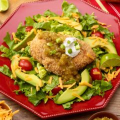 red plate holding one serving of Baked Panko Chicken, showing how to serve atop lettuce with garnishes on top and on the side