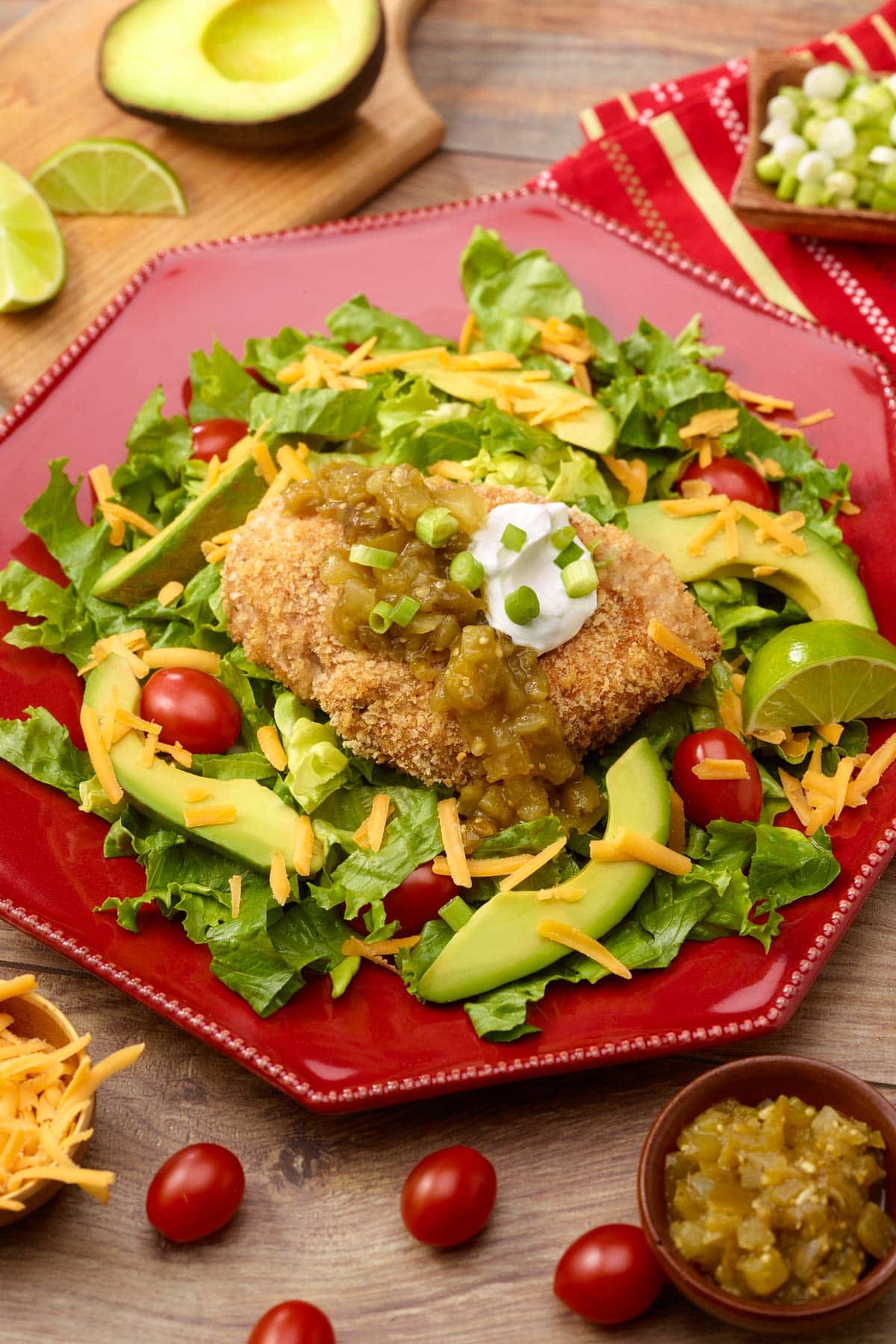 red plate holding one serving of Baked Panko Chicken, showing how to serve atop lettuce with garnishes on top and on the side