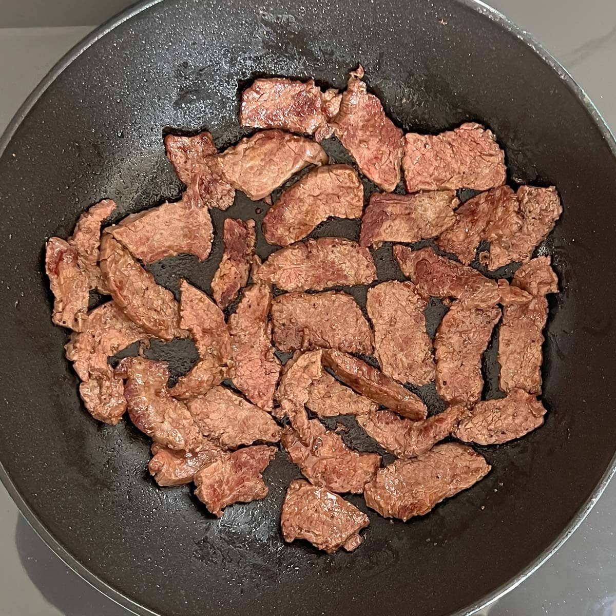 Sliced steak pieces cooked in a heated pan to make beef and broccoli stir-fry.