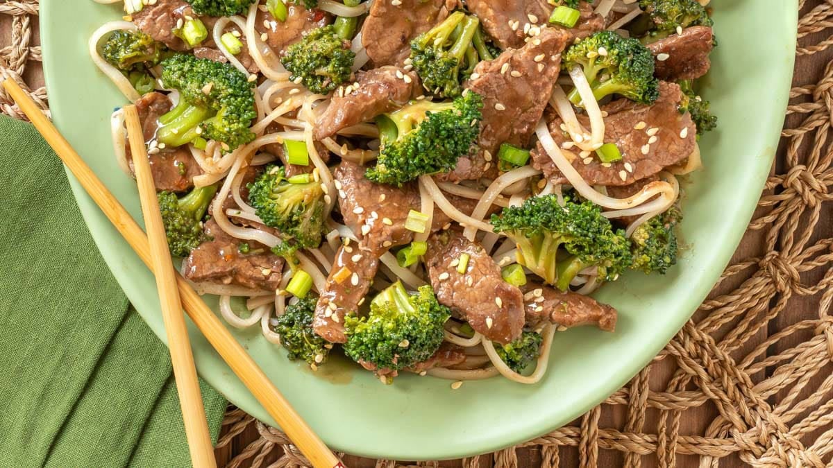 Easy beef and broccoli stir-fry with rice noodles, served on a light green platter with wooden chop sticks.