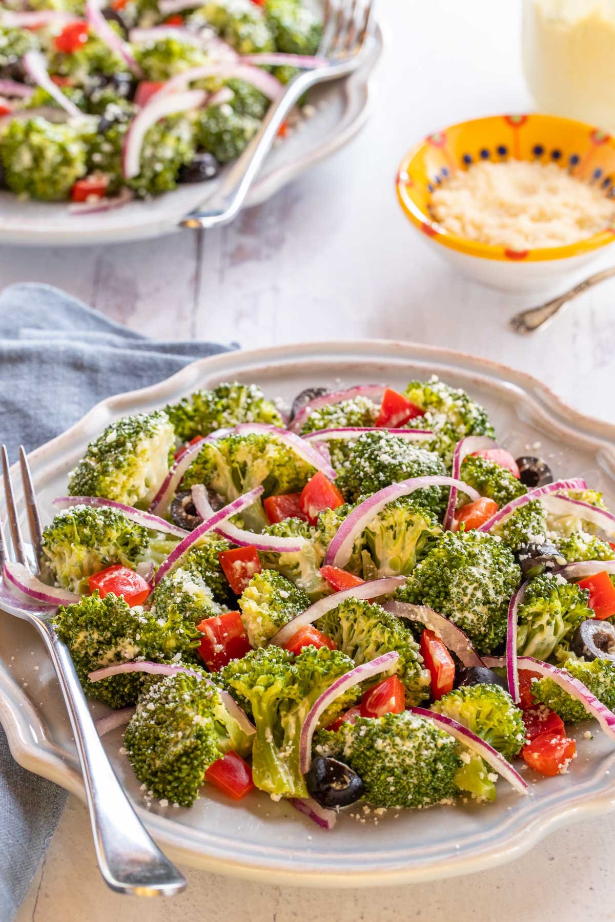 Blue plate displaying Best Broccoli Salad, with additional Parmesan Cheese on the side