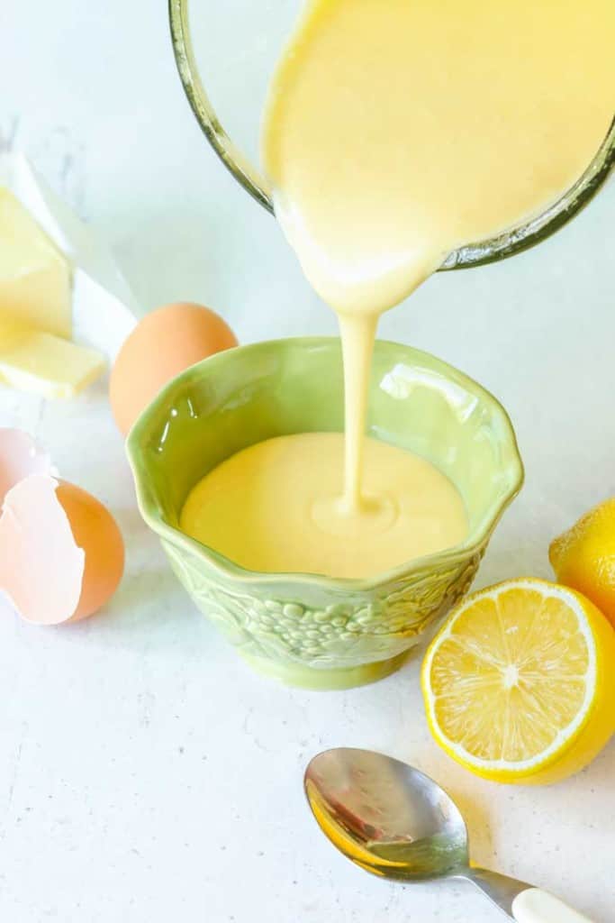 Blender pitcher pouring hollandaise sauce into a small green bowl that's surrounded by sauce ingredients