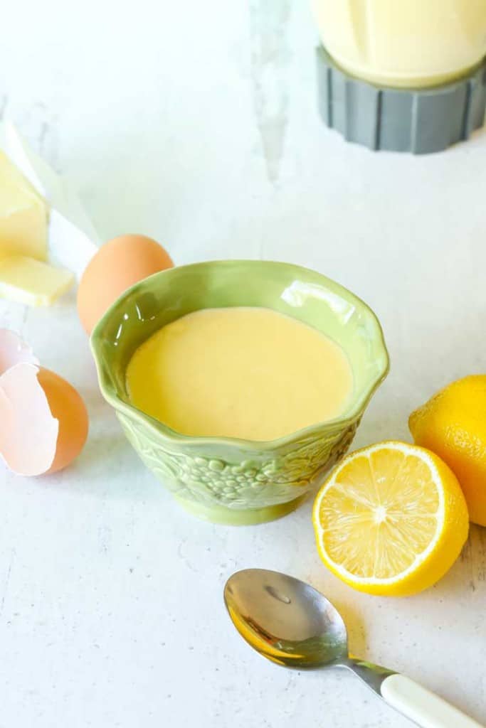 Small green bowl holding Hollandaise Sauce, surrounded by sauce ingredients