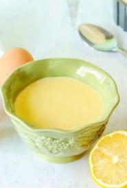 Small green bowl holding Hollandaise Sauce, surrounded by sauce ingredients