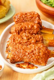 White platter holding 4 Spicy Beef Ribs with cornbread and salad in the back
