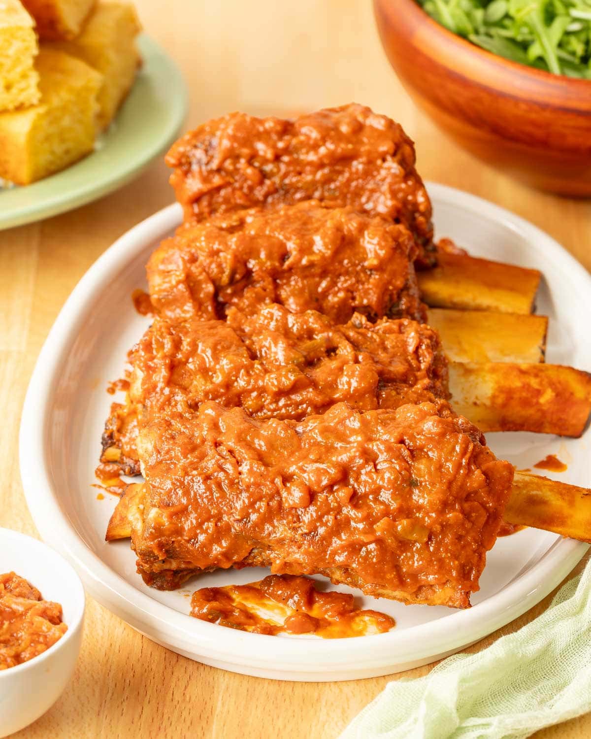 White platter holding 4 Spicy Beef Ribs with cornbread and salad in the back