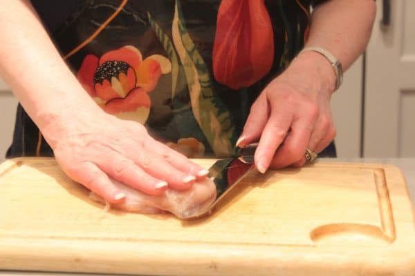 hands showing the first step in butterflying a chicken breast
