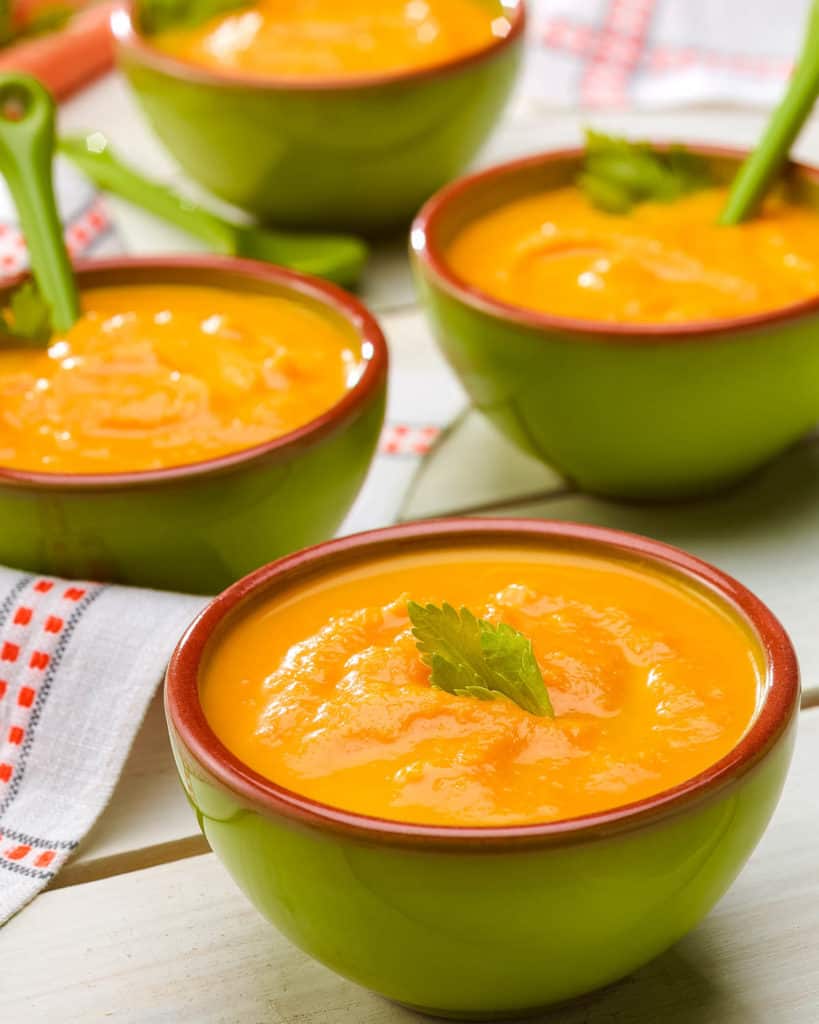 Three bowls of Creamy Carrot Ginger Soup with celery leaf garnish