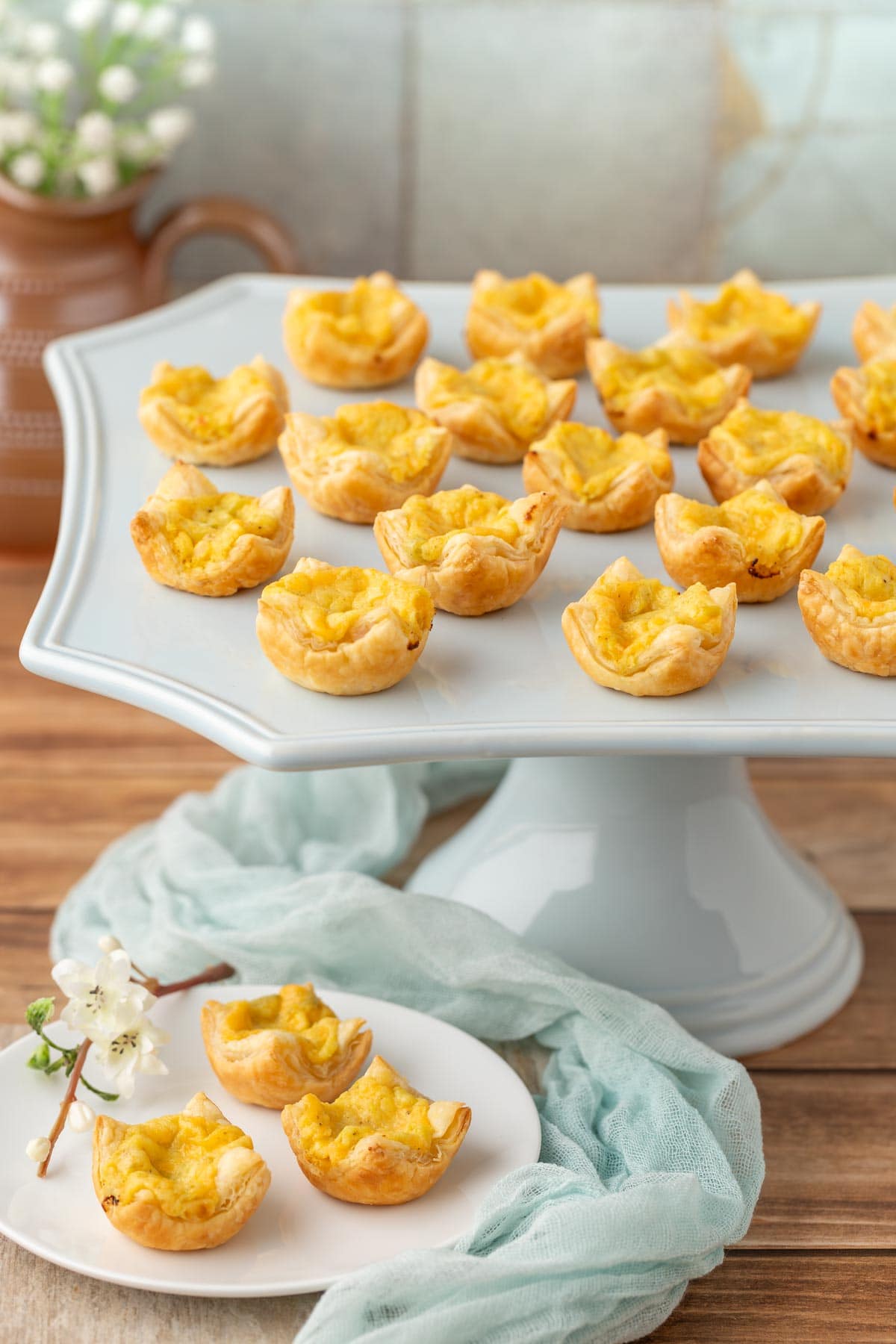 pale blue stand holding a portion of Mini Cheese Tarts with 3 on a plate in front
