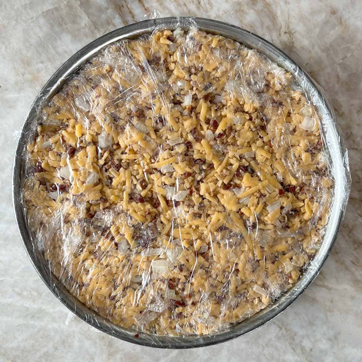 Spring form pan with final Cheddar mixture layer added, and the torte wrapped with plastic wrap