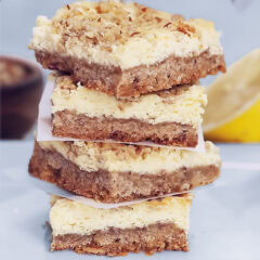 a stack of four Lemon Cheesecake Squares, with half of a lemon and a bowl of nuts in the background