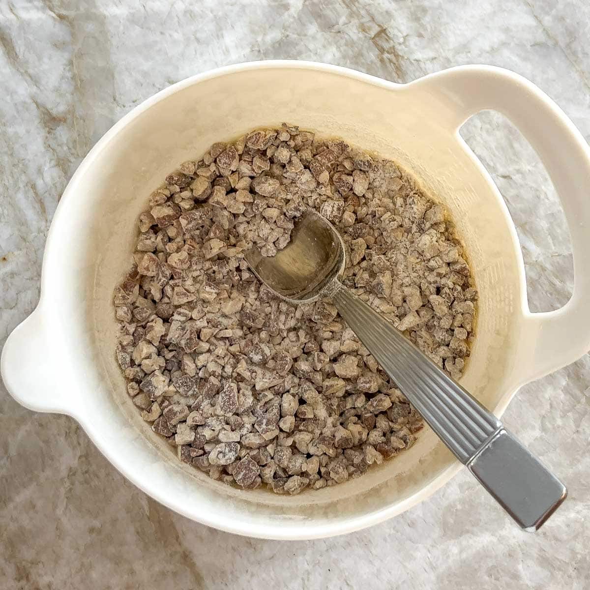 Mixing bowl holding mixture of flour, salt and toasted nuts with a spoon