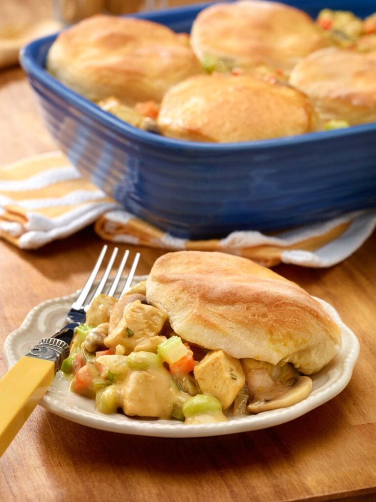 plate holding one portion of chicken pot pie with biscuits, with baking dish holding the rest in the background