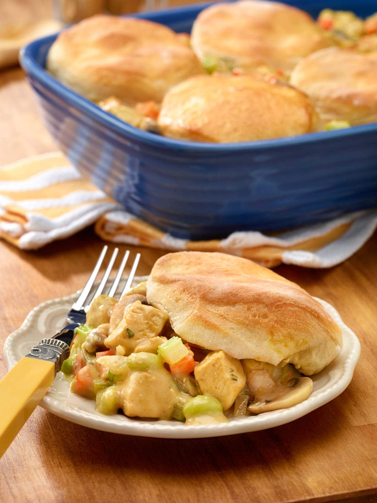 plate holding one portion of chicken pot pie with biscuits, with baking dish holding the rest in the background