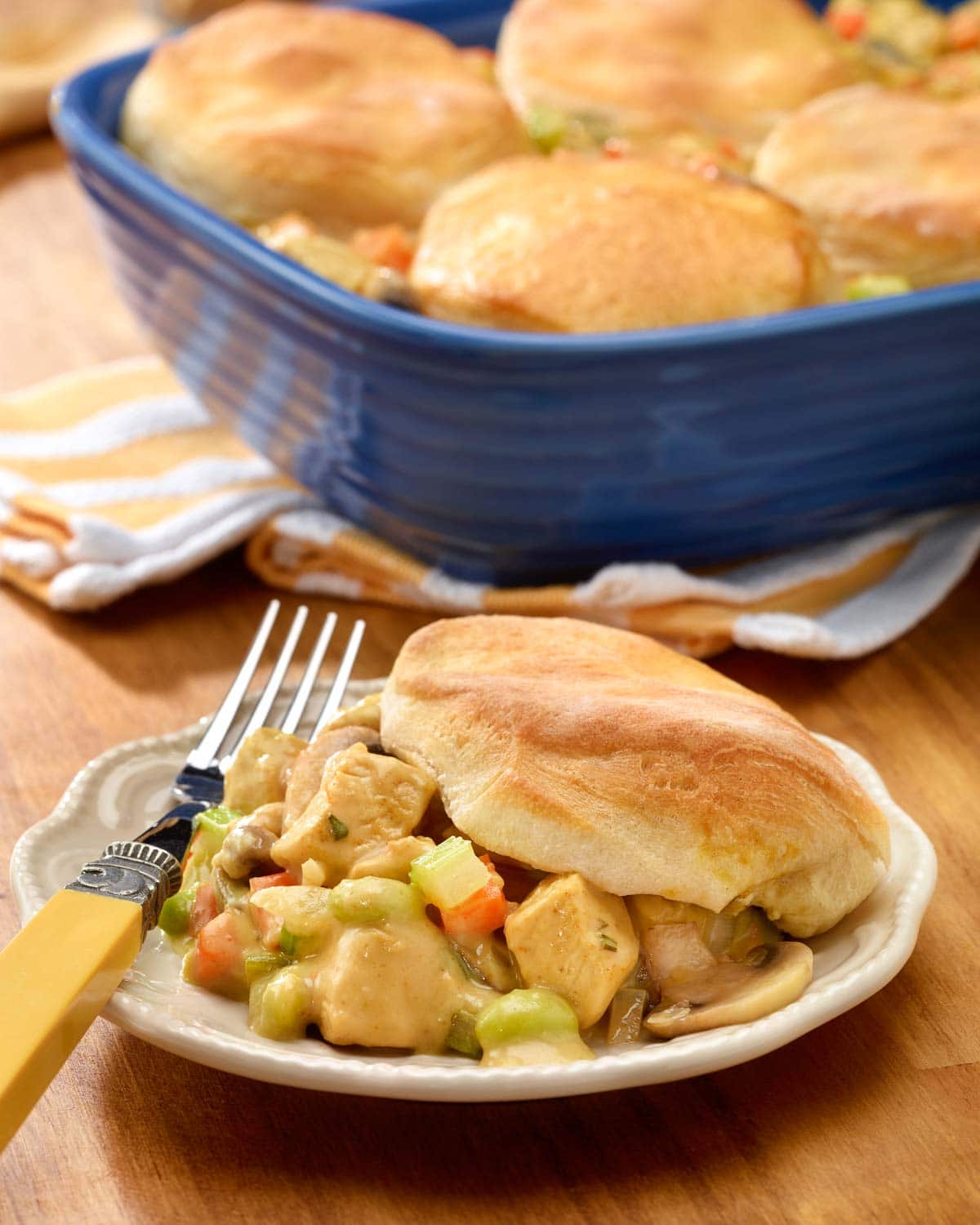 plate holding one portion of chicken pot pie with biscuits, with baking dish holding the rest in the background
