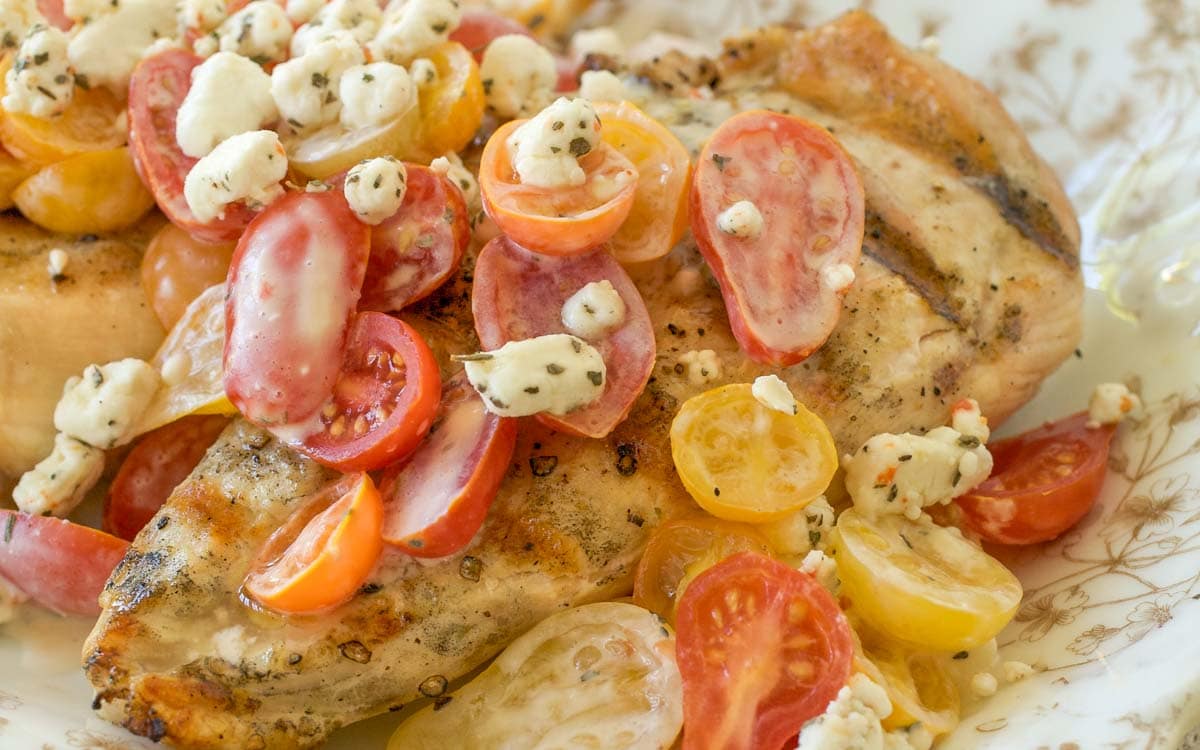 Close up of gold and white platter holding Grilled Chicken with Tomatoes and Goat Cheese
