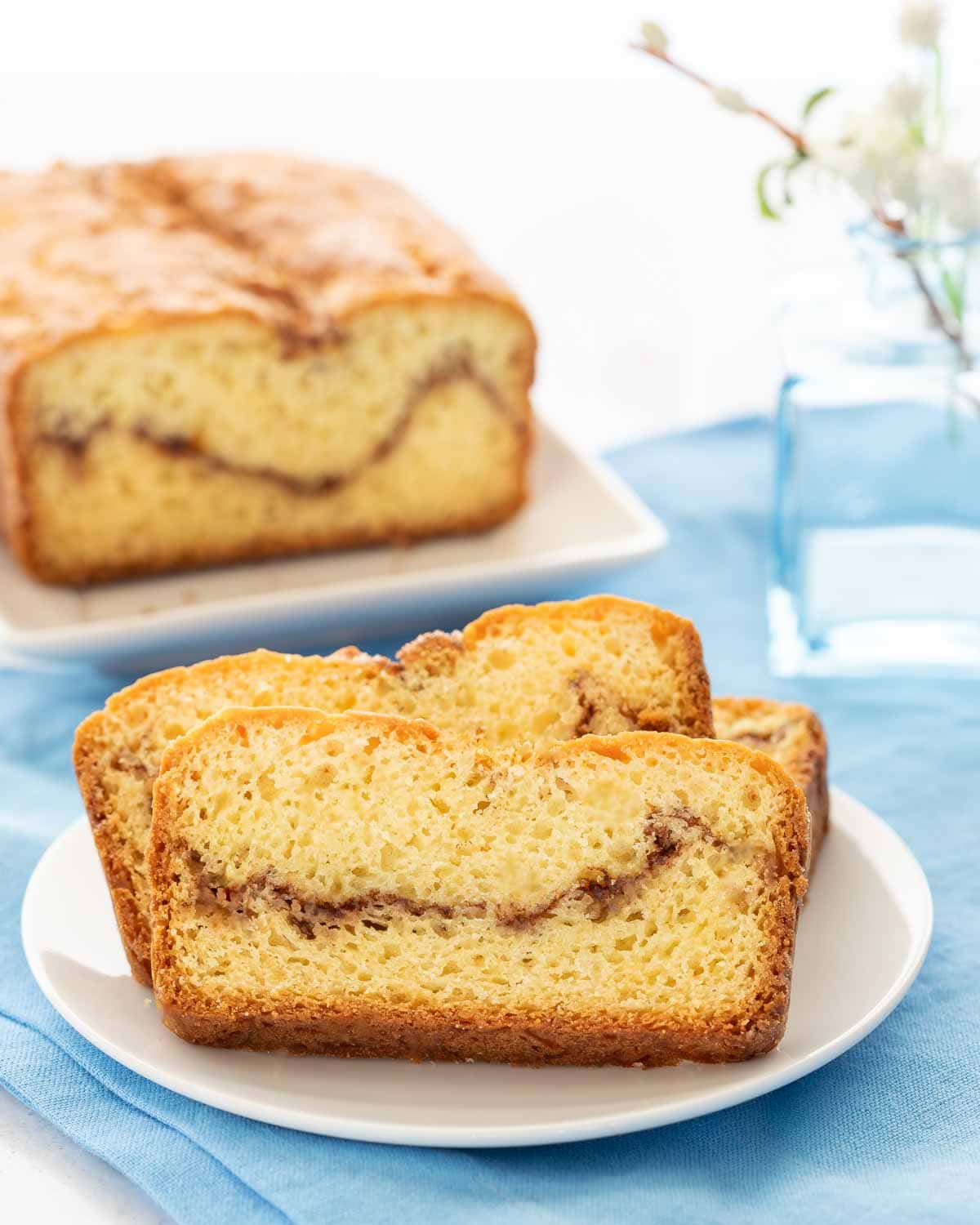 3 slices of Homemade Cinnamon Swirl Bread on a white plate, with the loaf behind