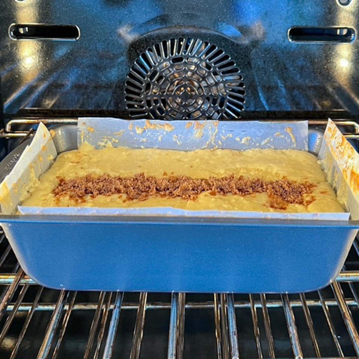 Batter in pan, in oven, showing the cut on top that's filled with cinnamon-sugar mixture