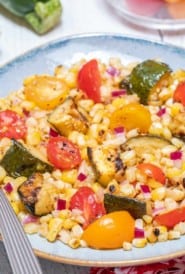 blue bowl holding grilled corn and zucchini salad with tomatoes
