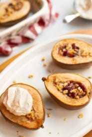 white oval plate with halved pears stuffed with cranberries and walnuts, topped with cinnamon whipped cream