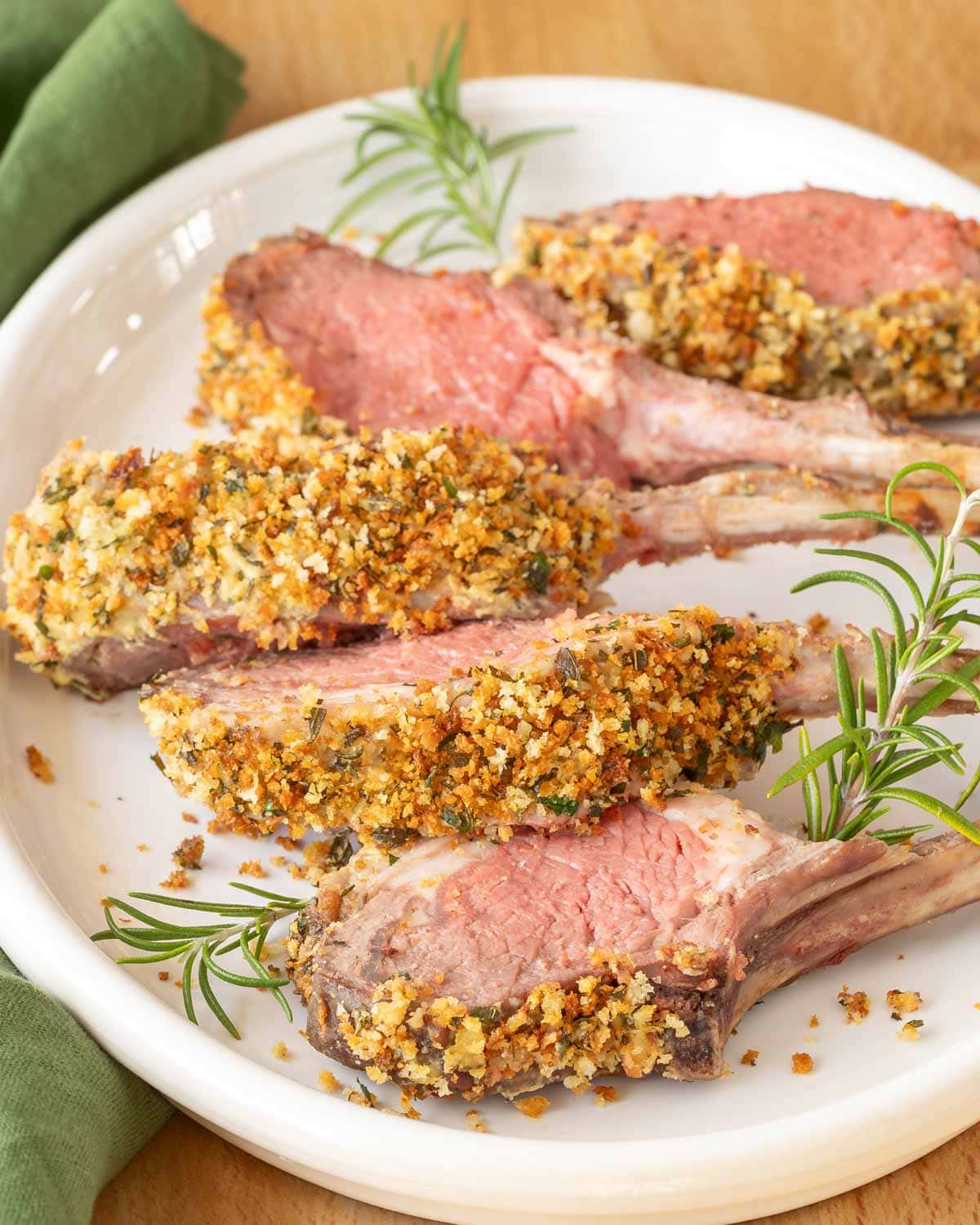 White platter holding individual chops from Crusted Rack of Lamb, with rosemary sprigs on edges