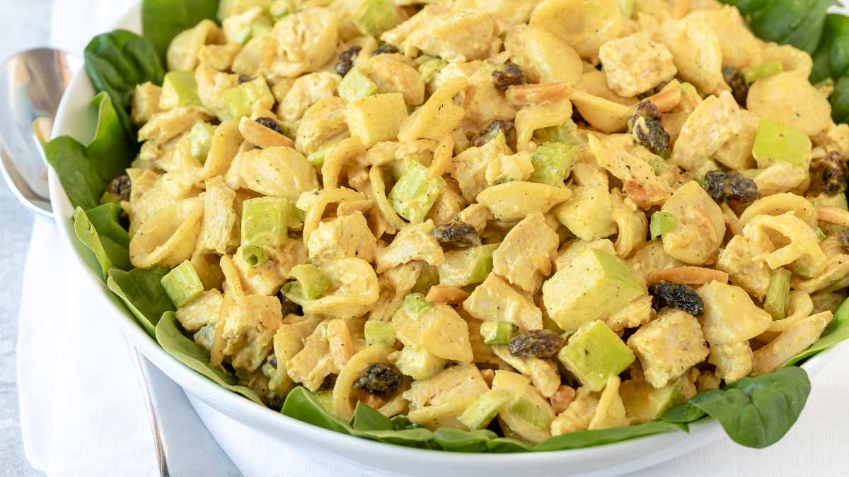 Close up of white bowl, lined with spinach leaved and filled with Curry Chicken Pasta Salad