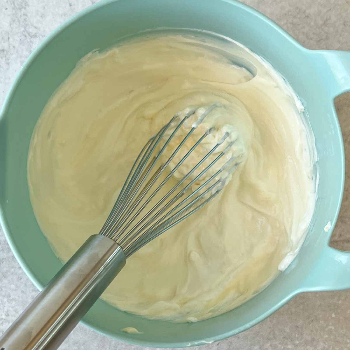 whisking mayo, sour cream, and yogurt for curry dressing in a blue bowl