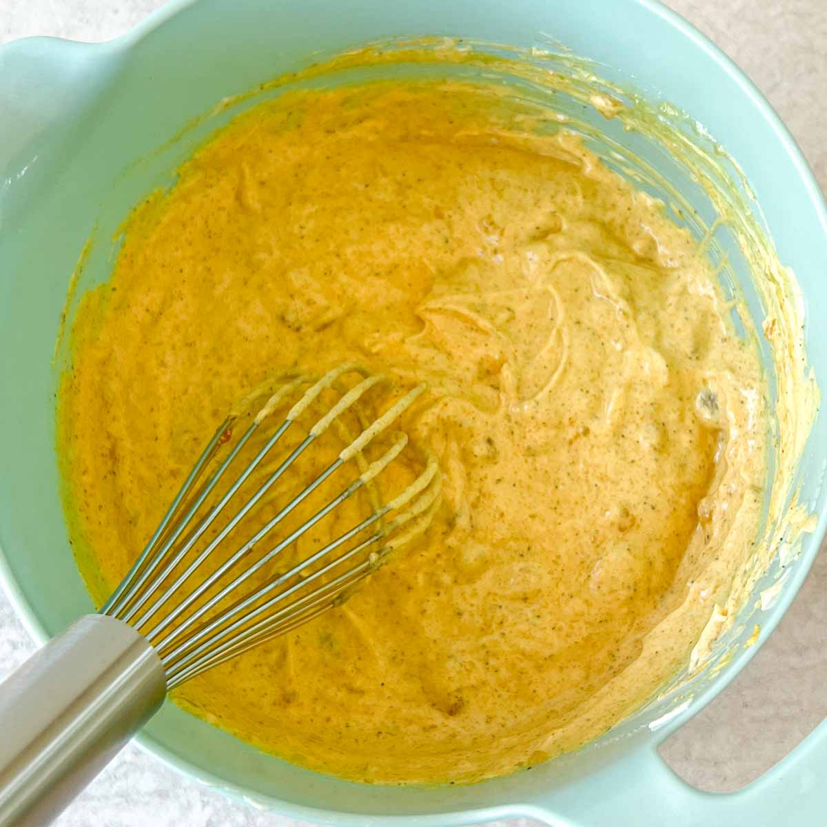 fully mixed curry dressing in a blue bowl with a whisk