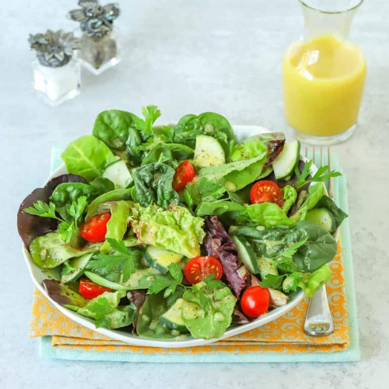 Plate holding a simple mixed green salad with a carafe of Dijon Vinaigrette alongside, along with small salt and pepper shakers