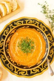 Overhead view of a bowl holding a portion of Roasted Eggplant Soup garnished with chives and bread on the side