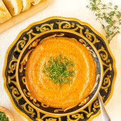 Overhead view of a bowl holding a portion of Roasted Eggplant Soup garnished with chives and bread on the side