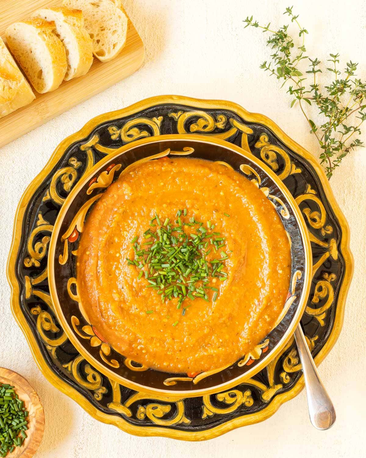 Overhead view of a bowl holding a portion of Roasted Eggplant Soup garnished with chives and bread on the side