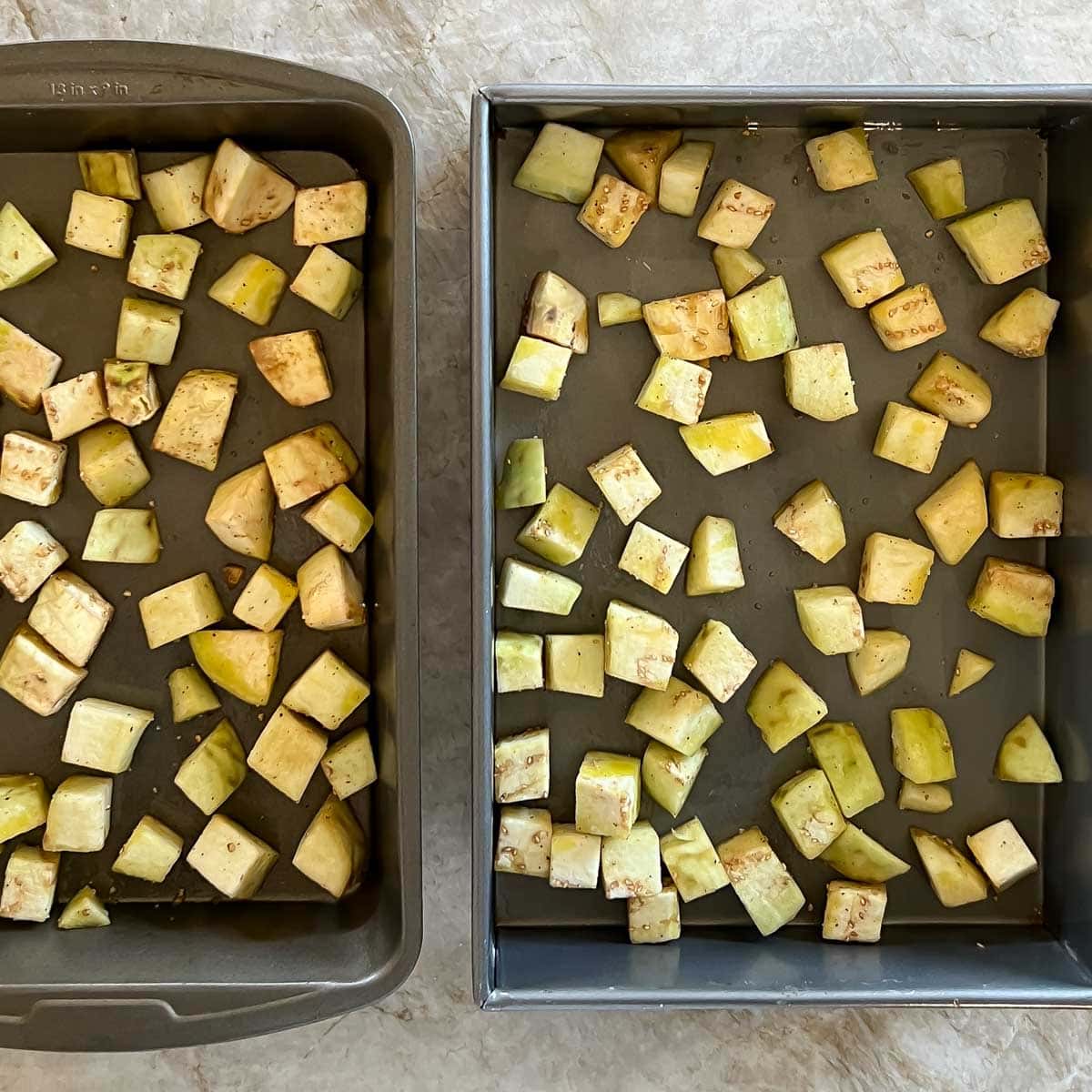 two roasting pans holding cubed eggplant ready for roasting