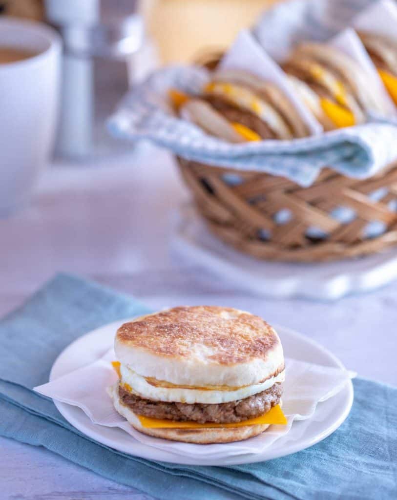 White plate showing a quick and easy Breakfast Sandwich with Egg; basket of sandwiches in the background