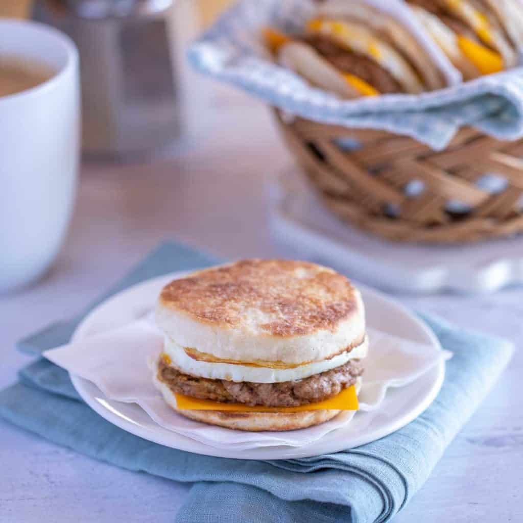 white plate showing an Egg Breakfast Sandwich, with basket of sandwiches and coffee in the background