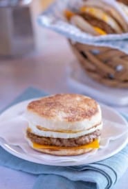 white plate showing an Egg Breakfast Sandwich, with basket of sandwiches and coffee in the background