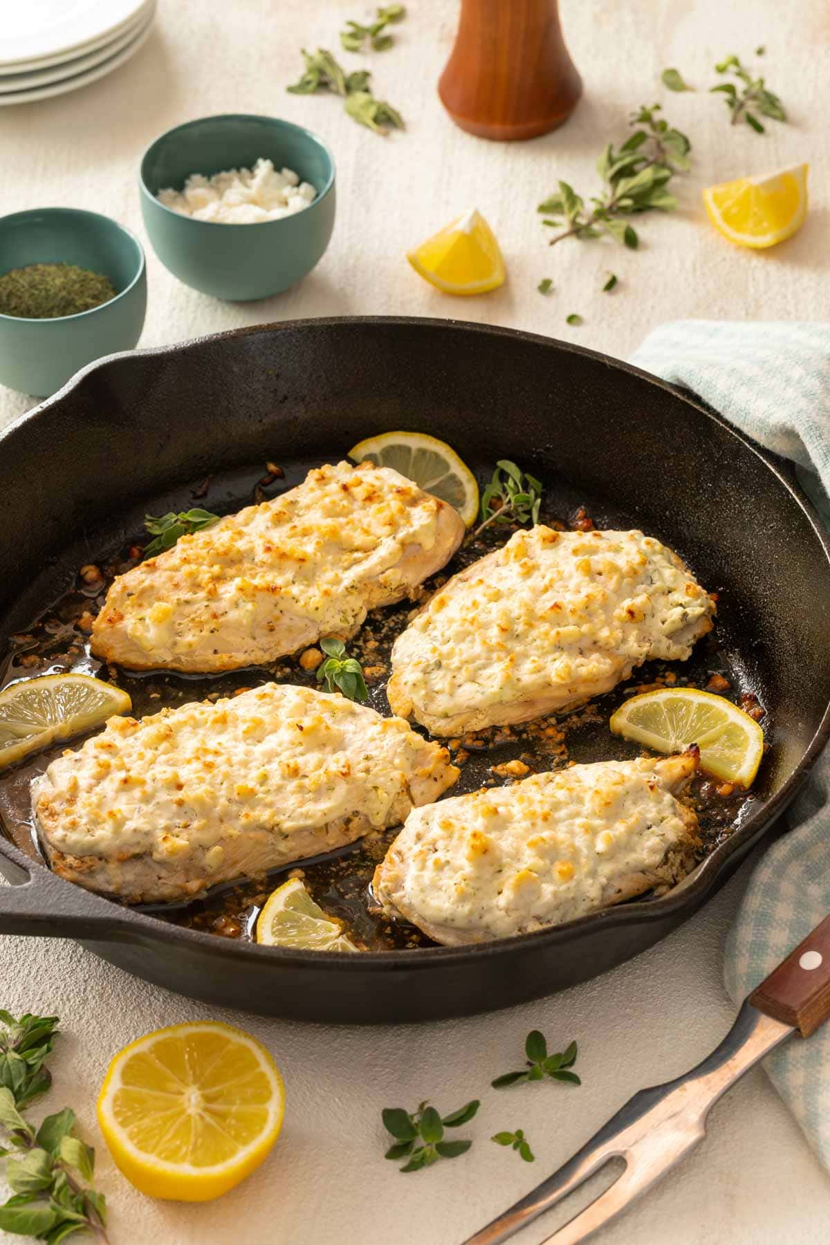 Cast iron skillet holding 4 Feta Chicken Breasts, with various ingredients surrounding the pan