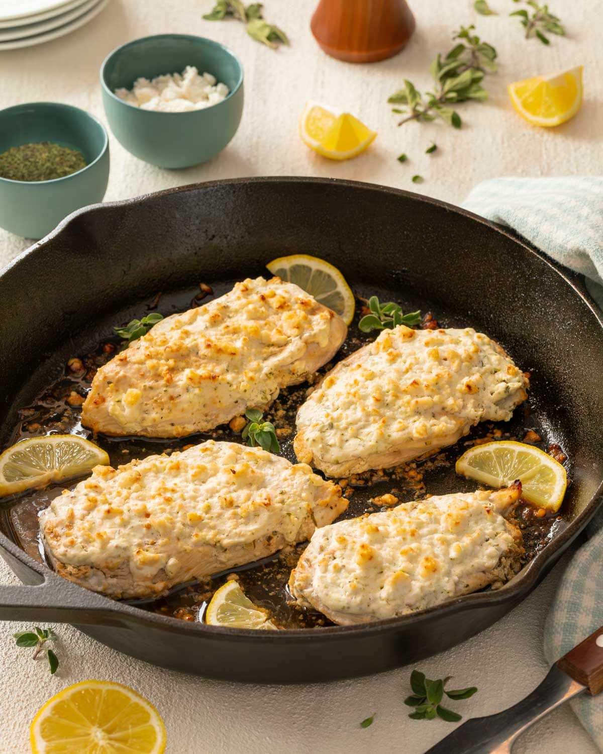 Cast iron skillet holding 4 Feta Chicken Breasts, with various ingredients surrounding the pan